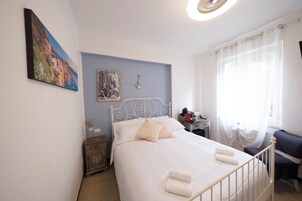 A bedroom with a bed, a nightstand, a chair, a desk, and a window with curtains.