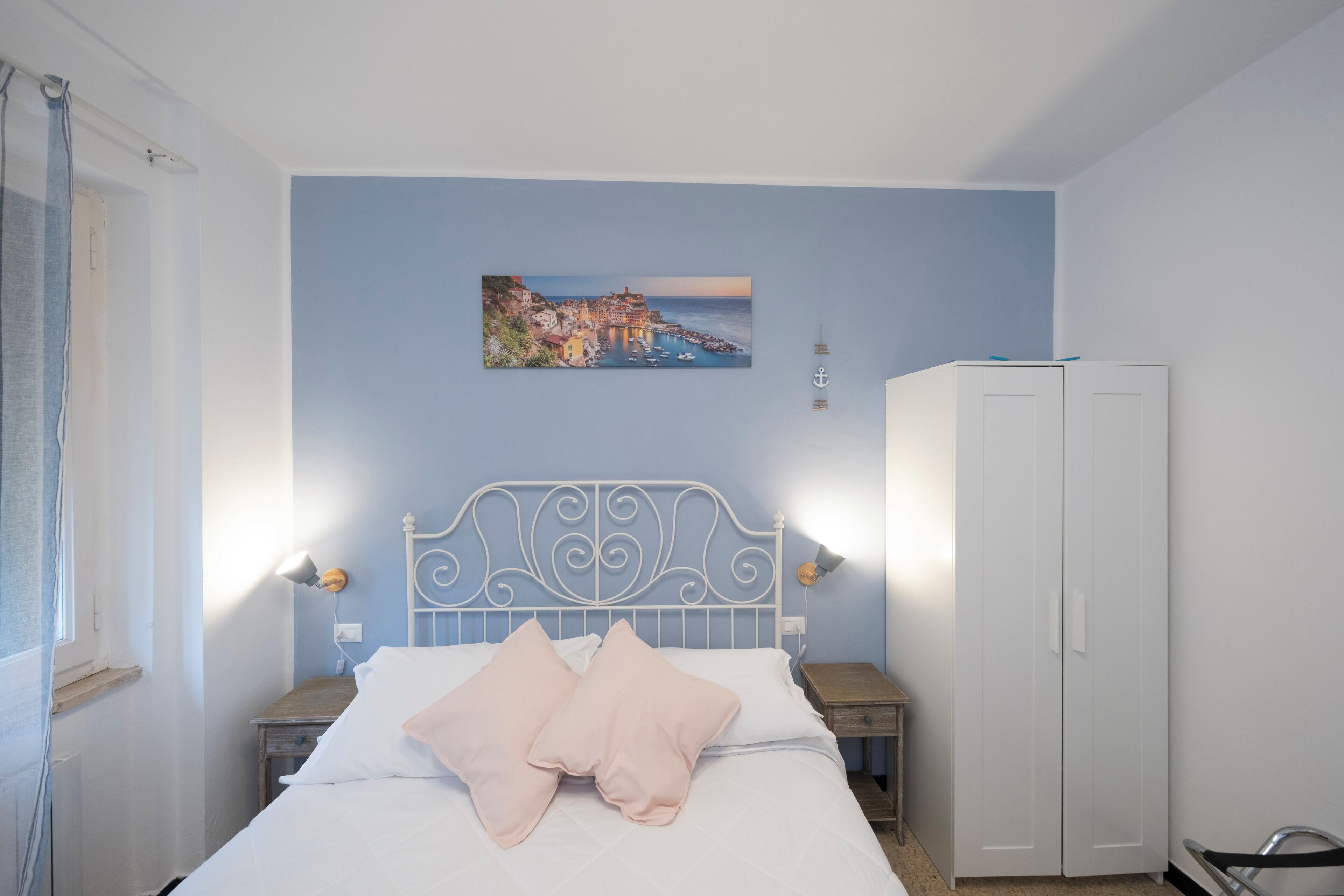 A bedroom with a bed, a nightstand, a wardrobe, and a wall-mounted picture.