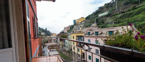 A balcony with a tiled floor, a railing, and a view of a hillside with buildings.