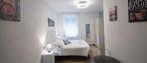 Un dormitorio con cama, mesita de noche, silla y obras de arte en las paredes.