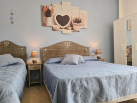 Un dormitorio con dos camas individuales, cabeceros de madera, mesitas de noche con lámparas, una obra de arte colgada en la pared y un armario.