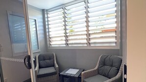 A room with a sliding glass door, two wicker chairs, a small table, and a window with blinds.