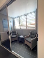 A room with a sliding glass door, two wicker chairs, a small table, and a window with blinds.