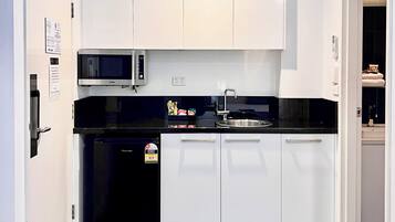 Una cocina compacta con armarios blancos, encimera negra, microondas integrado y refrigerador.