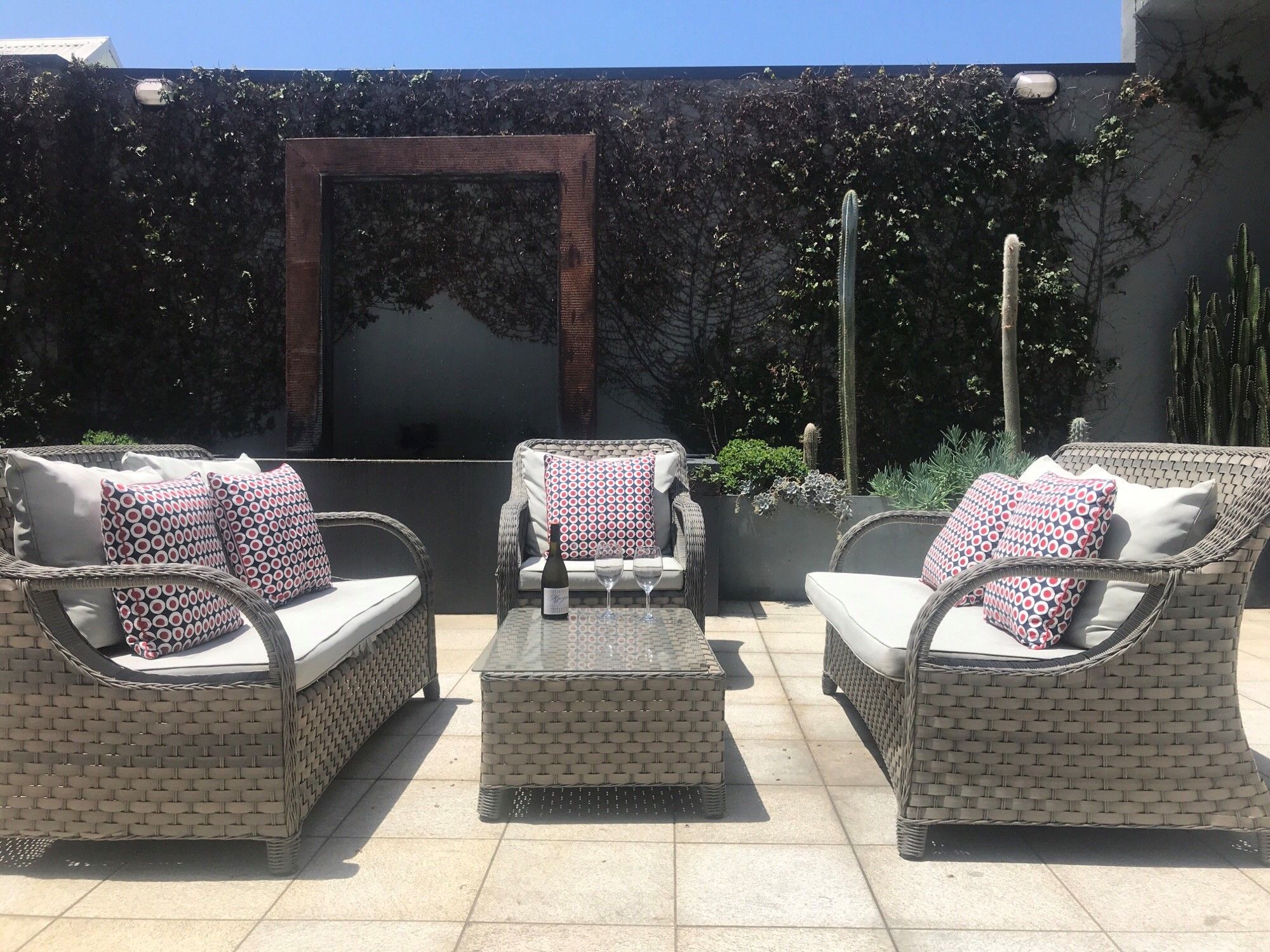 Un patio al aire libre con mobiliario de mimbre, incluyendo dos sofás y una silla, cada uno con cojines estampados.