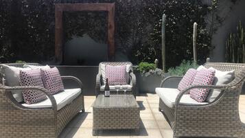 Un patio al aire libre con mobiliario de mimbre, incluyendo dos sofás y una silla, cada uno con cojines estampados.