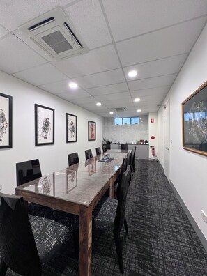 A conference room with a long table, chairs, framed artwork on the walls, and a kitchen area in the background. - Crown On Darby (Newcastle)