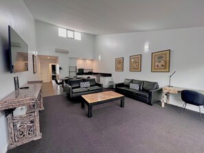 A modern living room with a sofa, coffee table, and a dining area with chairs. There is a kitchen in the background, a TV mounted on the wall, and framed pictures on the wall. - Crown On Darby (Newcastle)