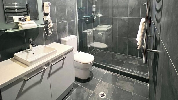 A modern bathroom with a glass-enclosed shower, a white sink, and a toilet. - Crown On Darby (Newcastle)