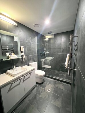 A modern bathroom with a glass-enclosed shower, a white sink, and a toilet. - Crown On Darby (Newcastle)
