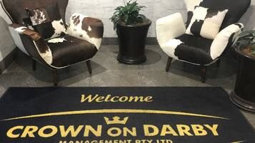 Two armchairs with a cowhide pattern, a potted plant, and a welcome mat with 'Crown on Darby Management Pty Ltd' text.