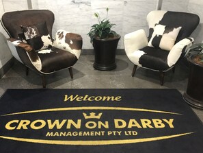 Dos sillones con estampado de piel de vaca, una planta en maceta y un felpudo con el texto 'Crown on Darby Management Pty Ltd'.