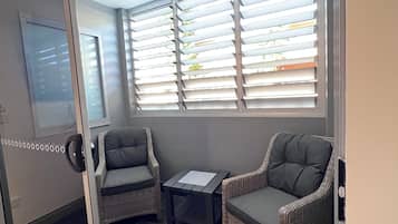 Una habitación con puerta de vidrio corrediza, dos sillas de mimbre, una mesita y una ventana con persianas.