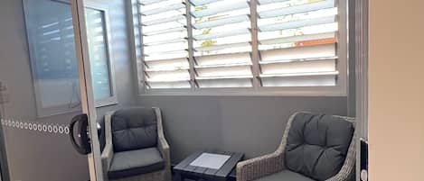 A room with a sliding glass door, two wicker chairs, a small table, and a window with blinds.