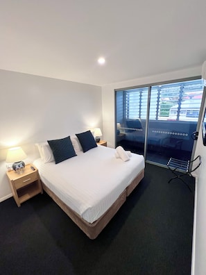 A hotel room with a bed, bedside tables, a lamp, a towel, and a view through a glass door. - Crown On Darby (Newcastle)