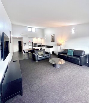 A modern living room with a sofa, a coffee table, and a dining area with chairs and a table. - Crown On Darby (Newcastle)