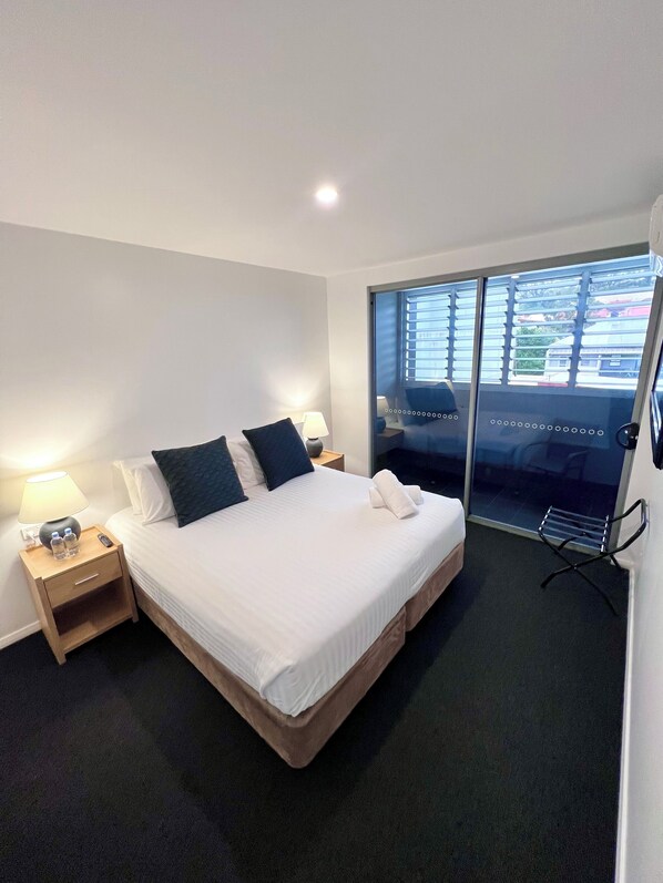 Une chambre d’hôtel avec un lit, des tables de chevet, une lampe, une serviette et une vue sur l’extérieur, visible à travers une porte vitrée.