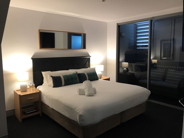 A hotel room with a large bed, two bedside tables with lamps, a mirror above the bed, and a sliding glass door leading to a balcony. - Crown On Darby (Newcastle)