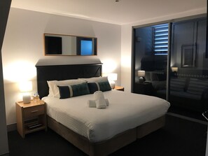 A hotel room with a large bed, two bedside tables with lamps, a mirror above the bed, and a sliding glass door leading to a balcony. - Crown On Darby (Newcastle)