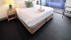 A hotel room with a large bed, two nightstands with lamps, a view of the outside through a sliding door, and two framed floral paintings on the wall. - Crown On Darby (Newcastle)