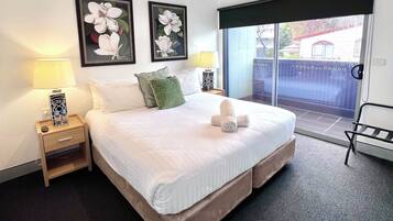 A hotel room with a large bed, two nightstands with lamps, a view of the outside through a sliding door, and two framed floral paintings on the wall.