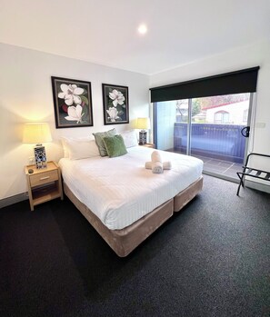 A hotel room with a large bed, two nightstands with lamps, a view of the outside through a sliding door, and two framed floral paintings on the wall. - Crown On Darby (Newcastle)