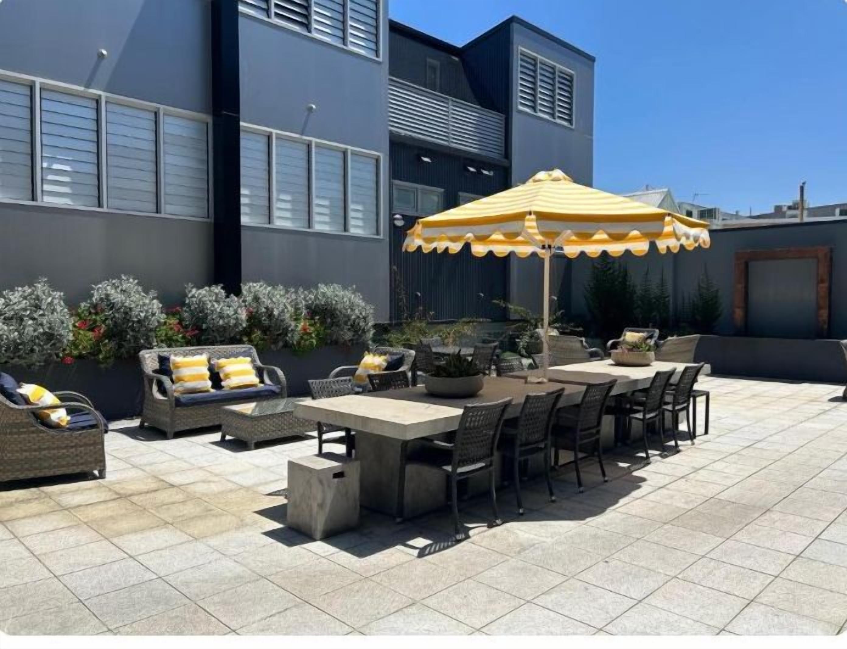 Una terrazza all'aperto con zona pranzo, posti a sedere e un ombrellone grande.