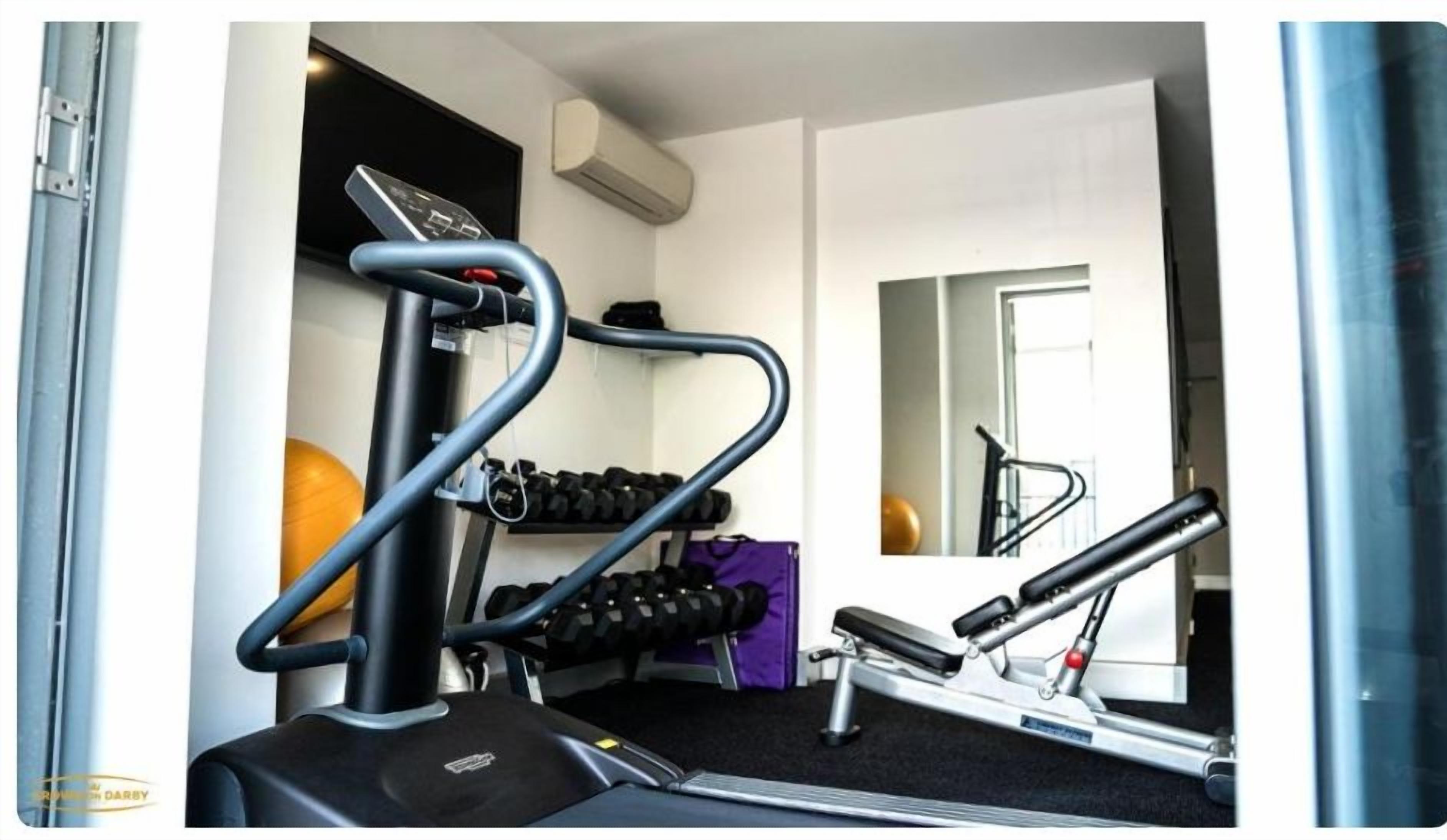Un gimnasio con equipo de cardio, mancuernas y un espejo.