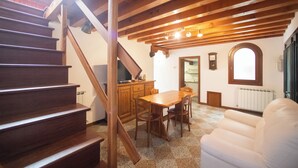 Una escalera de madera lleva a un comedor con una mesa y sillas, un sofá blanco y un reloj en la pared.