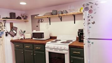 A kitchen with a microwave, stove, oven, and a refrigerator. There are shelves above the counter holding dishes and glasses.