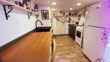 Eine Küche mit Holzboden, einem Esstisch, einer Spüle, einem Herd und einem Kühlschrank.