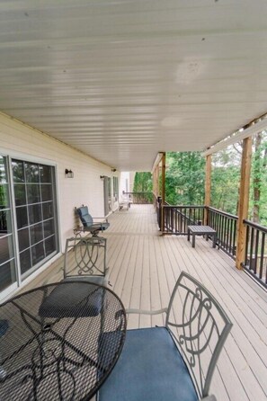 A covered porch with a table and chairs, large windows, and a view of trees.