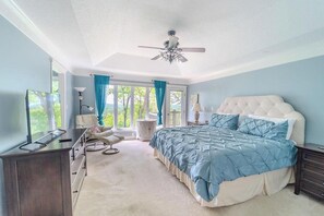 A bedroom with a large bed, a ceiling fan, a dresser, a chair, and a view of the outdoors.