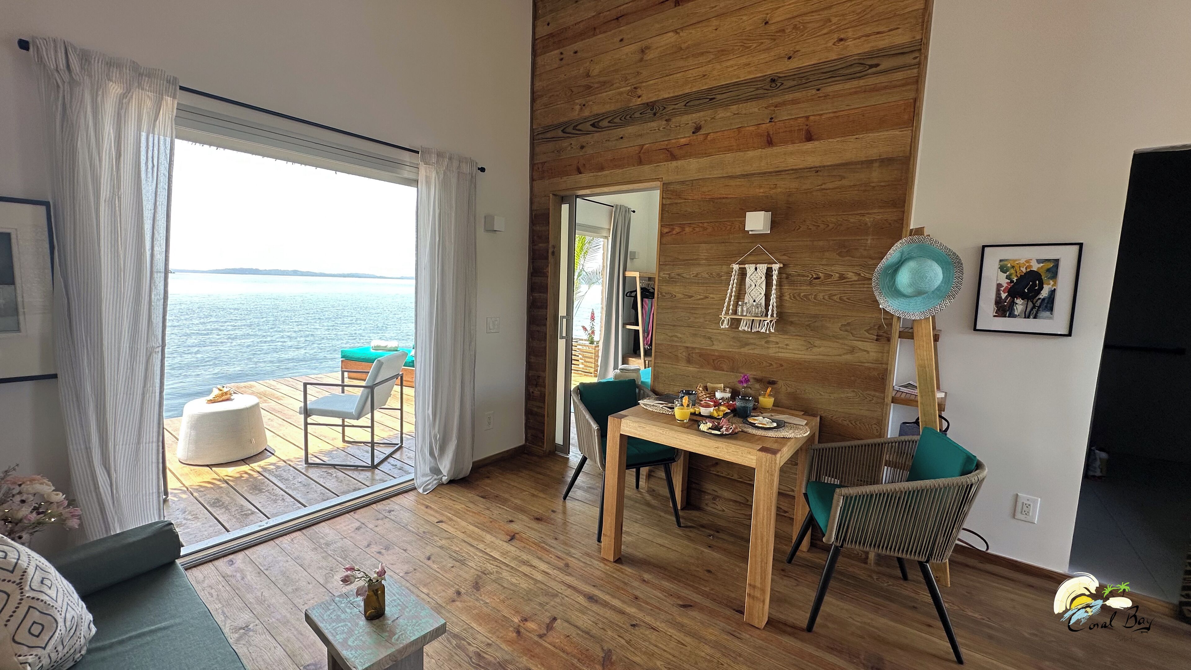Ein gemütliches Zimmer mit Holzboden, einem Esstisch mit Stühlen, Meerblick durch ein großes Fenster und einer Holzwand.
