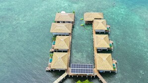 An aerial view of overwater bungalows with thatched roofs, connected by a wooden walkway, and a small boat in the water. - Ocean Breeze Over Water Bungalow, 1 Bedroom, 1 Kingbed, 1 Living Room, 1 Kitchen (Bastimentos Island)