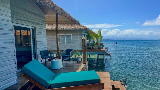 A wooden deck with lounge chairs and a thatched-roof structure overlooking clear blue water. - Ocean Breeze Over Water Bungalow, 1 Bedroom, 1 Kingbed, 1 Living Room, 1 Kitchen (Bastimentos Island)