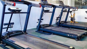 Trois tapis de course fixes dans une pièce dotée d’une grande fenêtre et d’un mur recouvert de miroirs.
