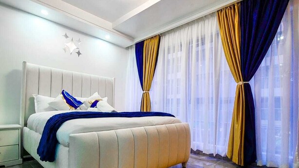 Une chambre à coucher moderne avec un grand lit, un tapis orange moelleux et des rideaux aux motifs bleus et dorés.