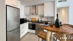 A modern kitchen with white cabinets, stainless steel appliances, and a wooden dining table with chairs. - ETERNA Apartment in Moraira – 100 metres from the beach, 2 bedrooms, air conditioning and Wi-Fi (Moraira)