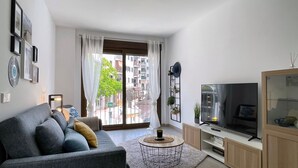 A modern living room with a sofa, TV, and a large window with curtains. - ETERNA Apartment in Moraira – 100 metres from the beach, 2 bedrooms, air conditioning and Wi-Fi (Moraira)