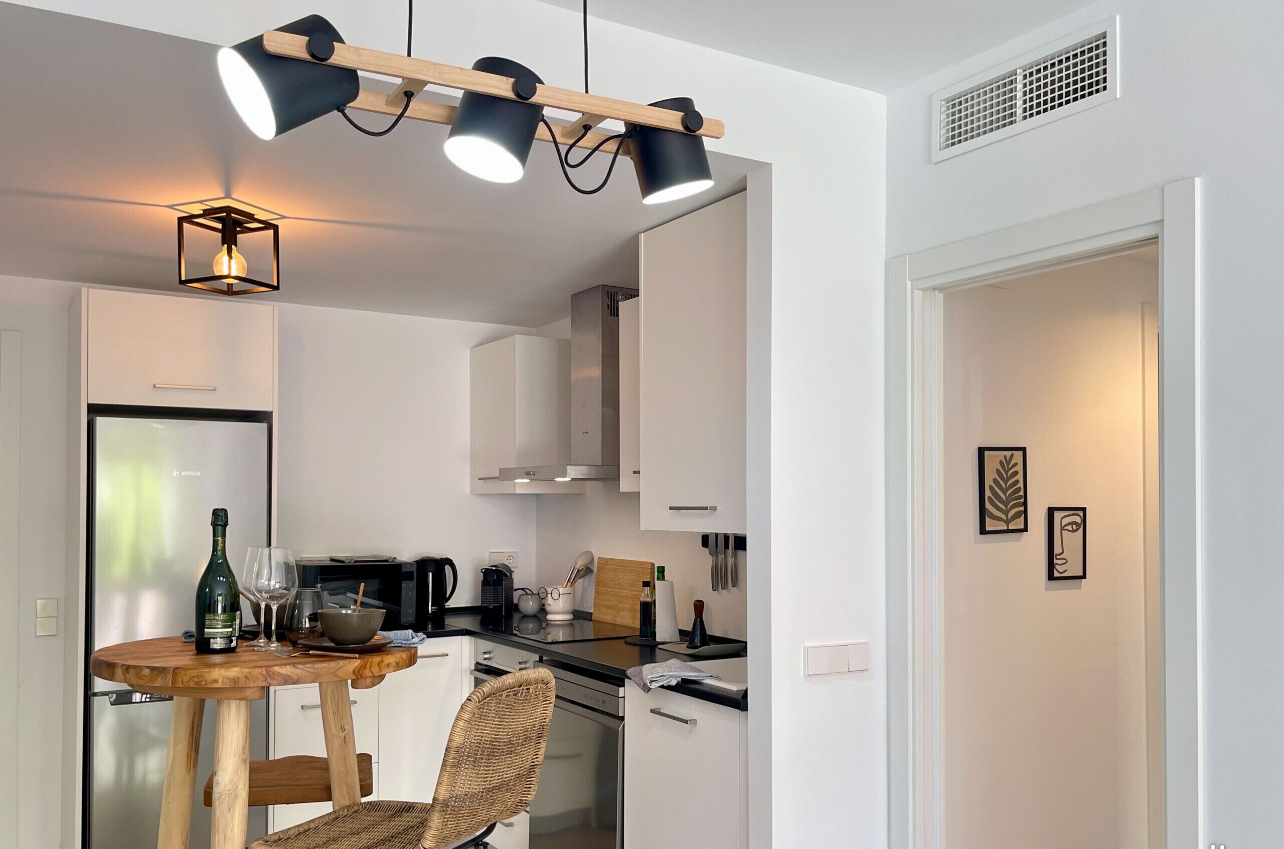 A modern kitchen with white cabinets, a wooden dining table, and a hanging light fixture.