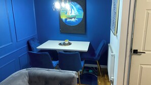 A room with blue walls, a white table, and blue chairs. There is a painting of a sailboat on the wall, a radiator, and a door. - Home Away From Home! Lovely House Near M1 (Nottingham)