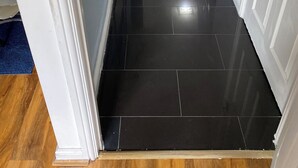 A hallway with black tiled flooring, white walls, and a wooden floor at the end. - Home Away From Home! Lovely House Near M1 (Nottingham)