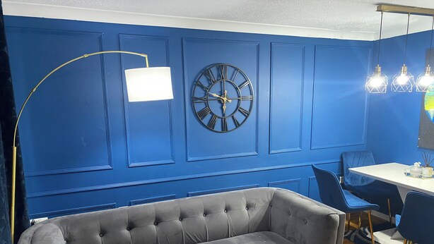 A room with a blue wall, a grey sofa, a white table, and a black clock. - Home Away From Home! Lovely House Near M1 (Nottingham)