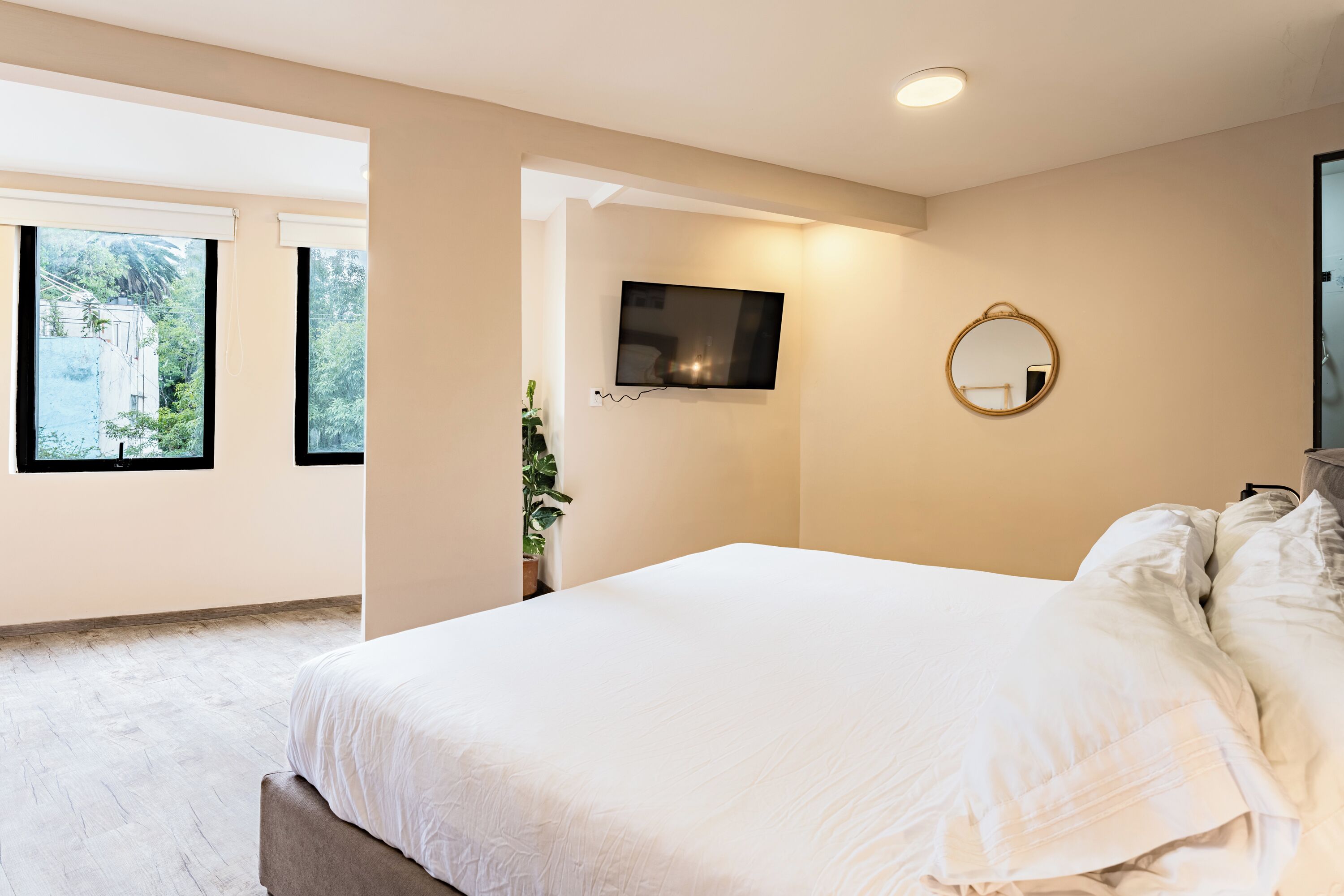 Une chambre moderne avec un grand lit, un téléviseur fixé au mur et une fenêtre donnant sur un paysage verdoyant.