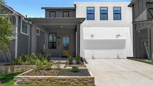 Une maison moderne à deux étages, dotée d’un garage, d’une porte d’entrée et d’un jardin bien entretenu où poussent différentes espèces de plantes.