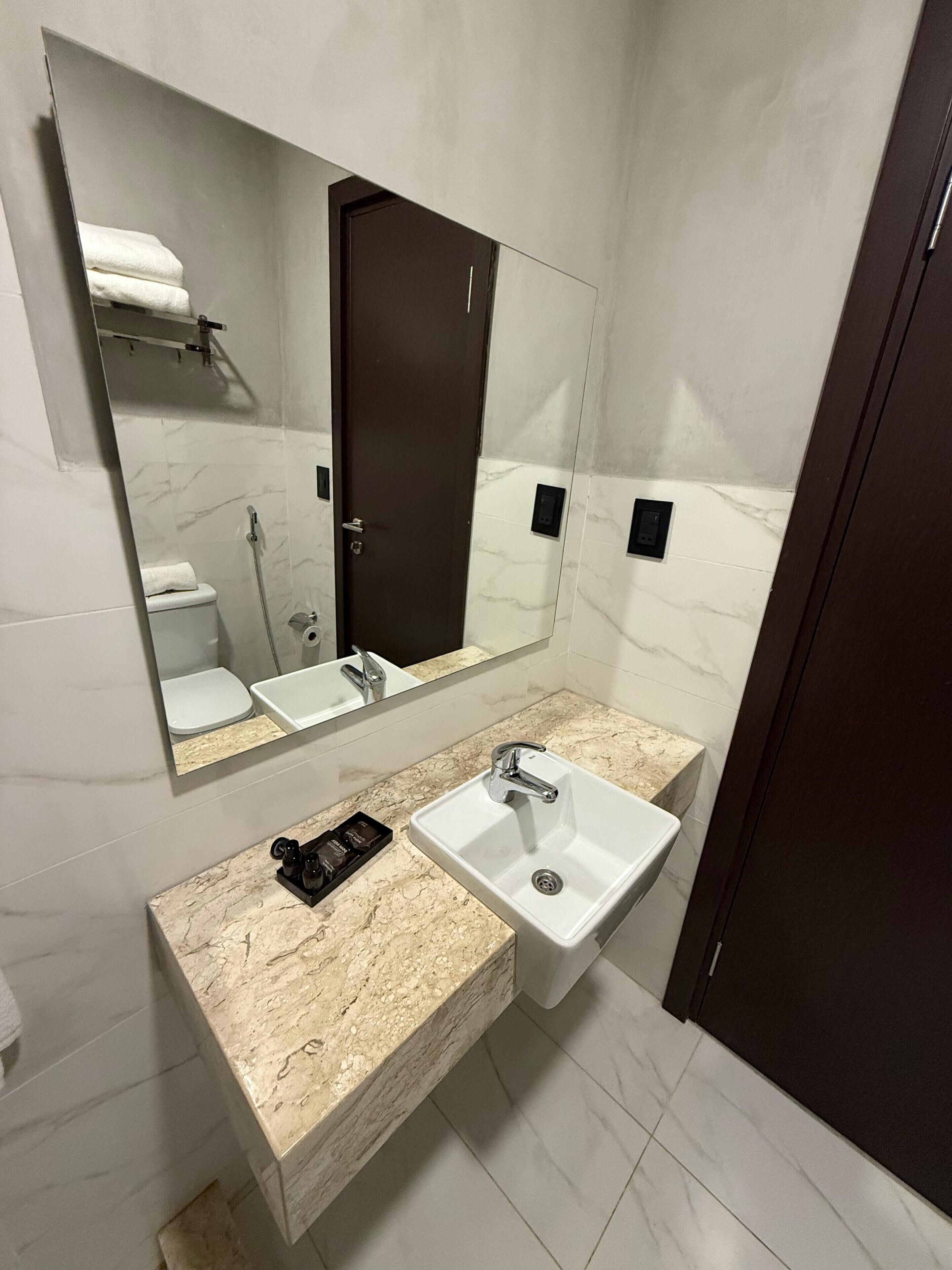 Un baño moderno con tocador de mármol, lavamanos, espejo y retrete.