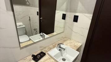 Un baño moderno con tocador de mármol, lavamanos, espejo y retrete.
