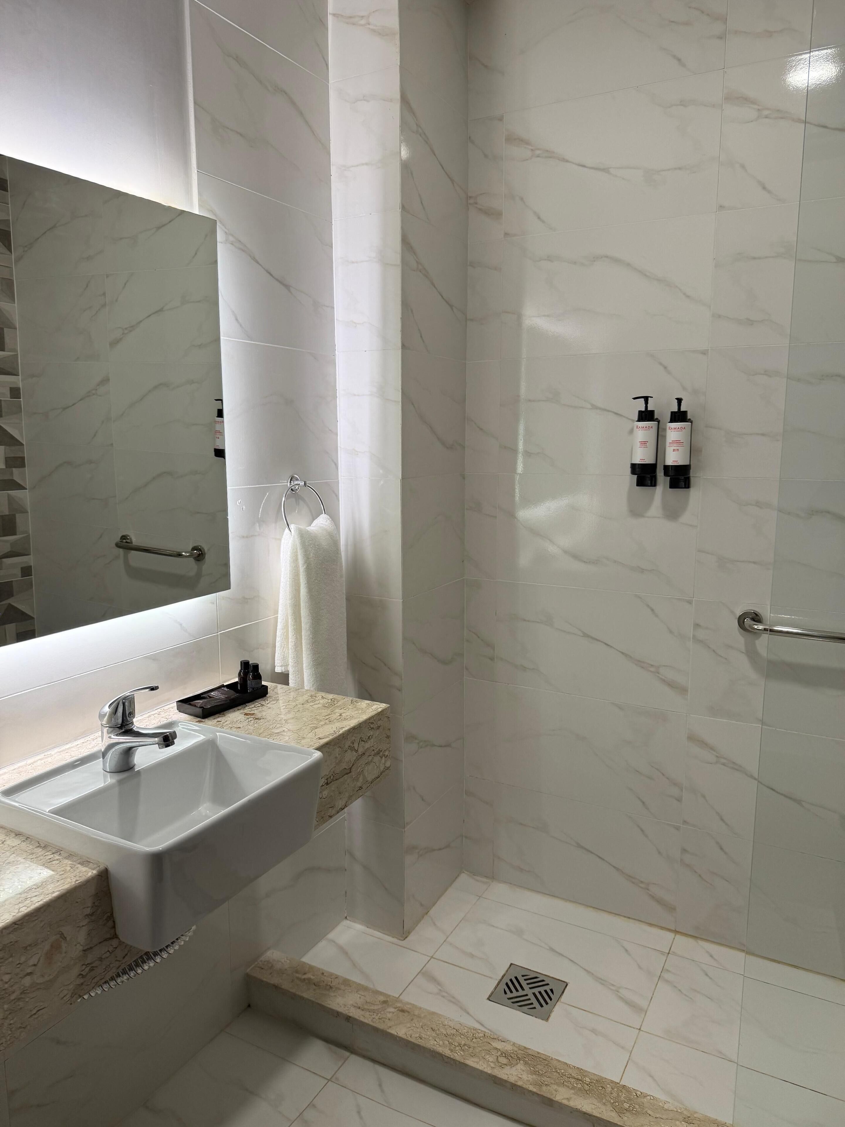 A modern bathroom with a marble sink, a large mirror, and a shower area.
