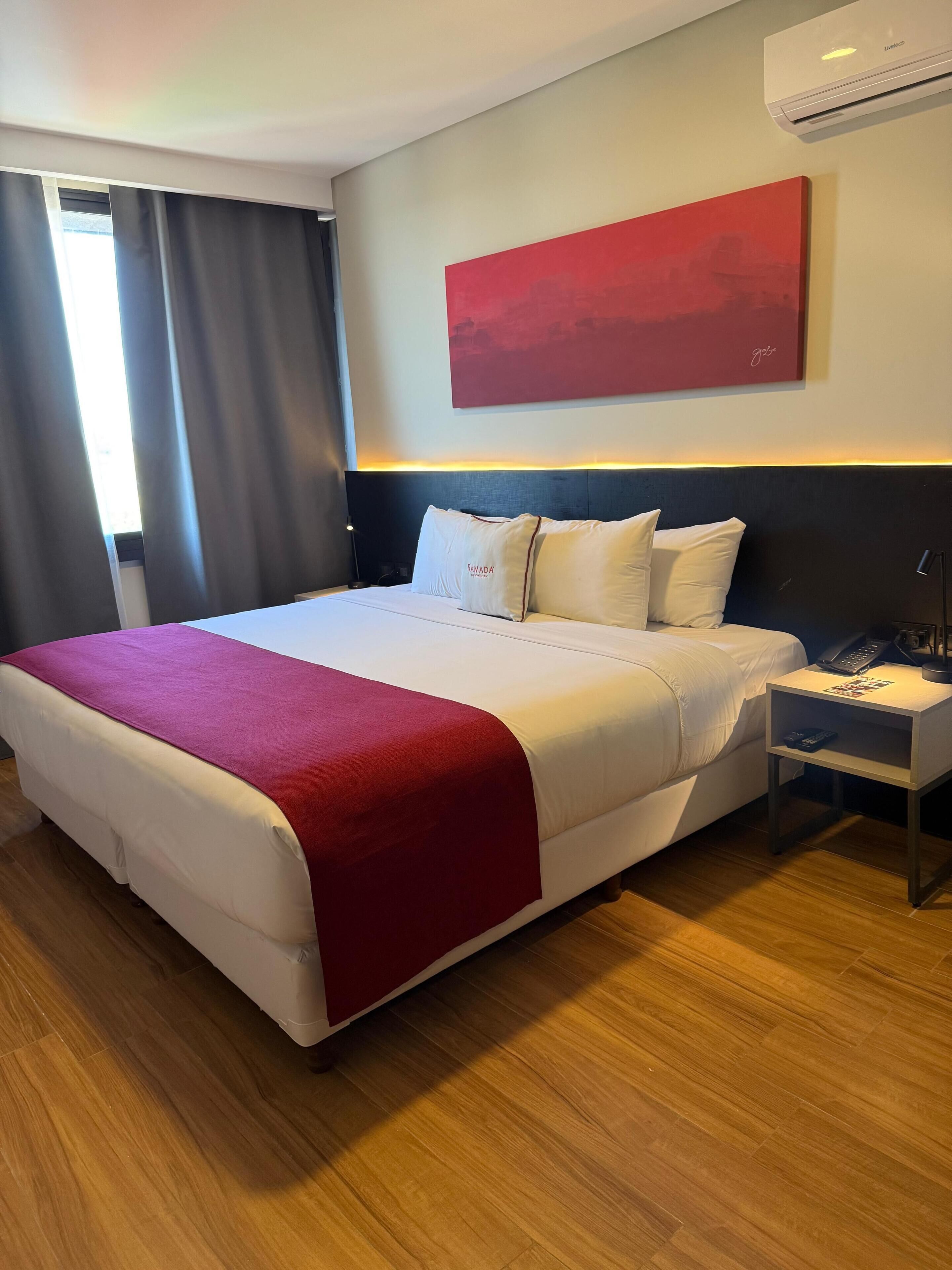 Una camera d'albergo con un letto grande, un comodino con il telefono e un quadro astratto rosso appeso alla parete.
